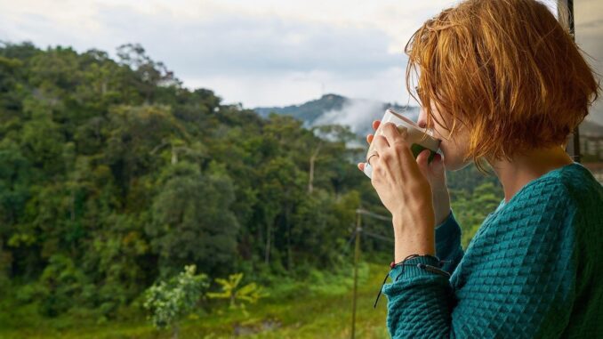 žena z profilu pije raní kávu na balkoně