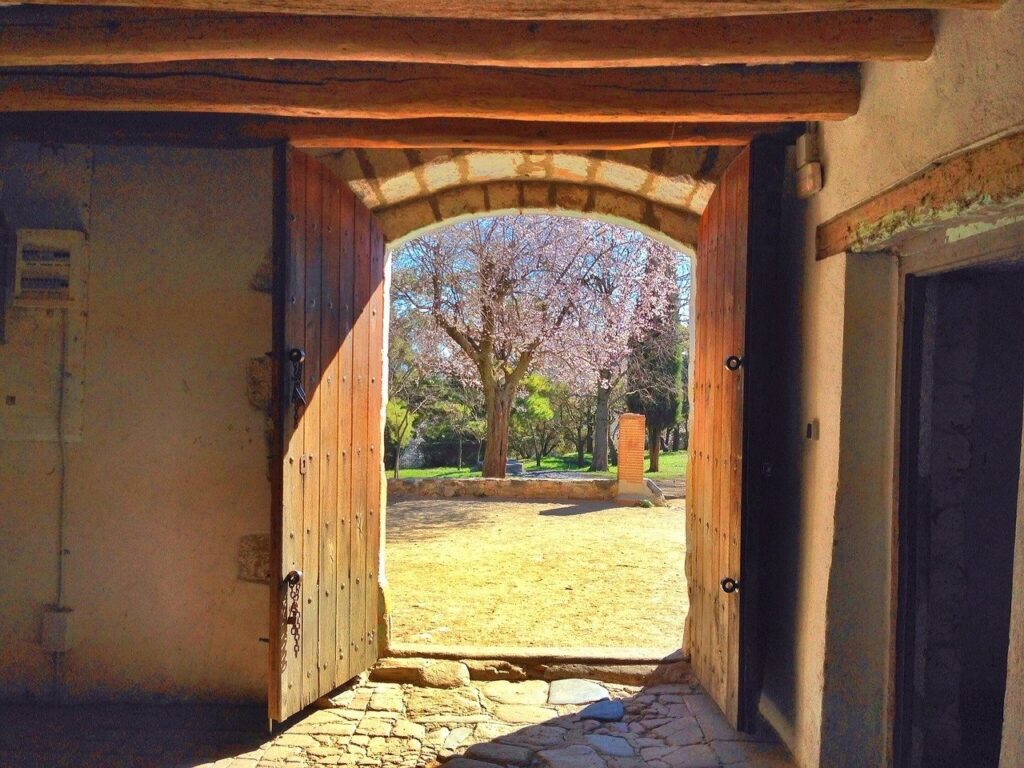 Otevřené dveře starého grunt za kterými je vidět zahrada s rozkvetlou třešní.