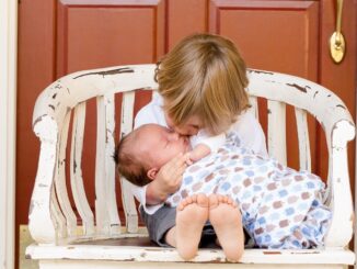 Dvě děti na laviččce, jede z nich je novorozené miminko.