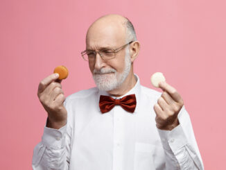 Starší muž drží v každé ruce jednu sušenku.