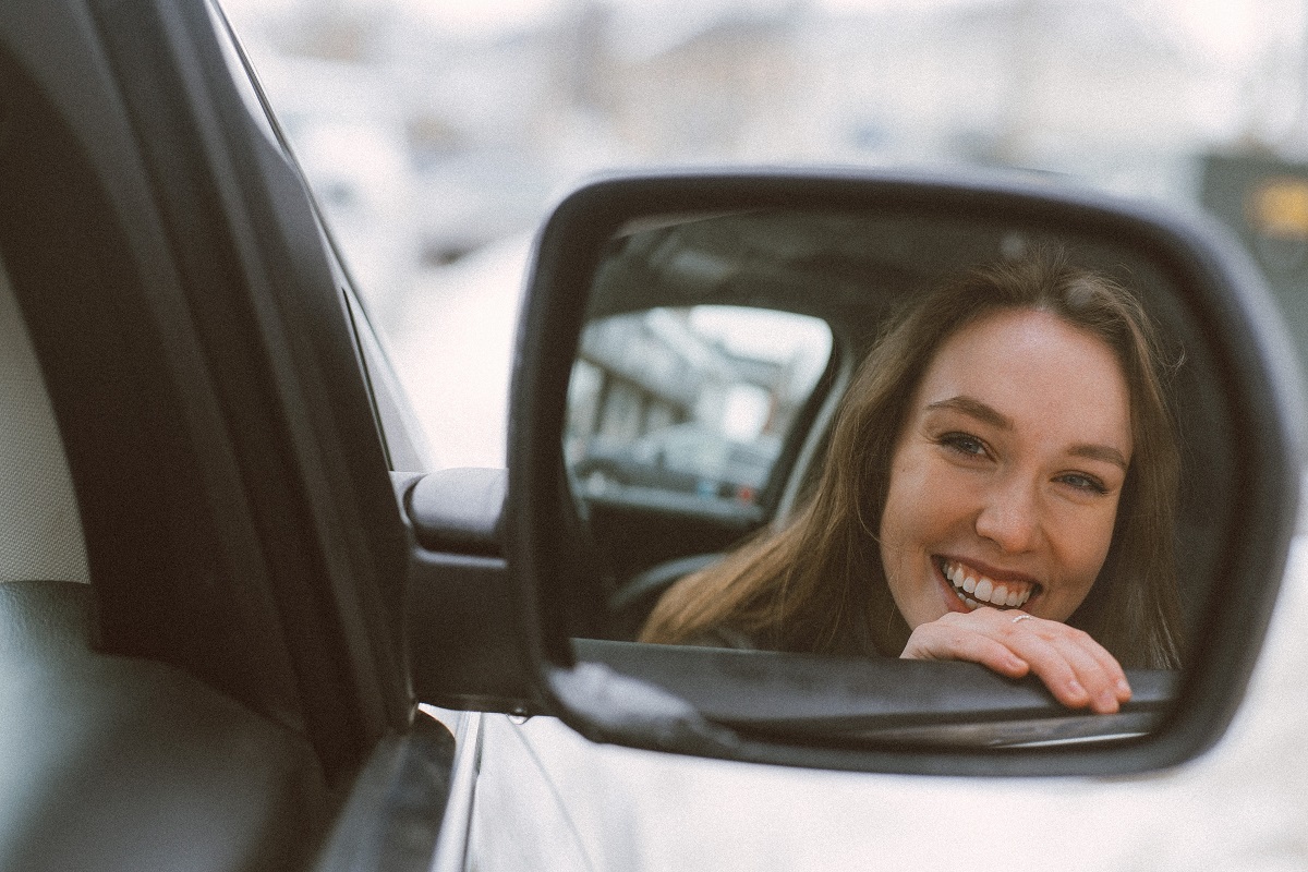 zrcadlo na autě ve kterém je vidět usměvavá žena.